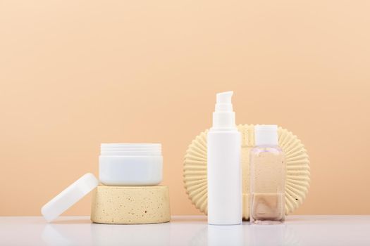 Set of beauty products, white opened jar on podium and tube with cream and lotion against beige background with copy space. Concept of natural skin care