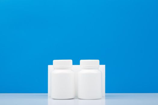 Two white medication bottles against blue background with copy space. Concept of healthcare and medical treatment or vitamins. High quality photo