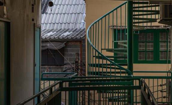 Bangkok, Thailand - 25 Jan 2020 : Green spiral staircase pattern in old apartment. Spiral stairs circle in courtyard architecture. Outdoor ladder decoration interior. Selective focus.