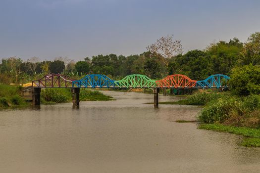 A contemporary coloured metal rainbow bridge over a canal. Arch bridge. Selective focus.