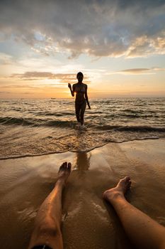 Woman silhouette on the beach at sunset with man legs.