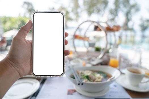 Woman hands holding blank screen mockup phone, order food online concept, breakfast background.