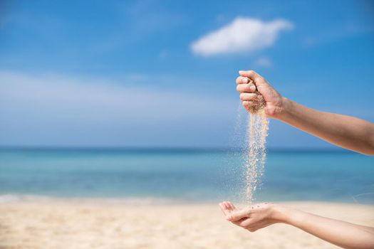 Woman pouring the sand from hand to hand on the beach, blue sky.