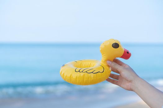 Hand holding a yellow duck on the beach with a sea in the background.