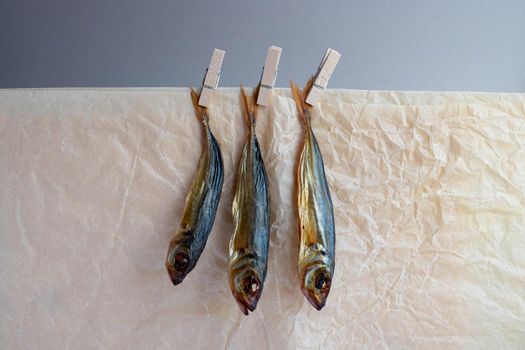 Smoked horse mackerel close-up hanging on clothespins on a crumpled paper background .