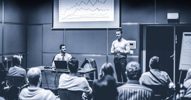 Speaker giving a talk in conference hall at business event. Unrecognizable people in audience at conference hall. Business and Entrepreneurship concept. Blue toned black and white.