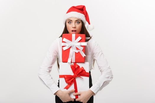 Business Concept - Beautiful young caucasian business woman with santa hat holding a lot of gift boxes with surprising facial expression.