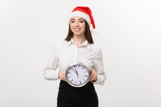 Time management concept - Young happy business woman with santa hat holdinga clock isolated over white background.