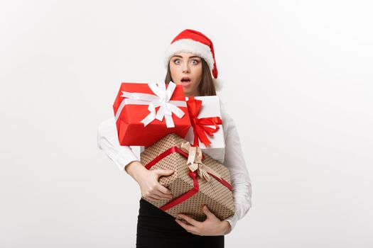 Business Concept - Beautiful young caucasian business woman with santa hat holding a lot of gift boxes with surprising facial expression.