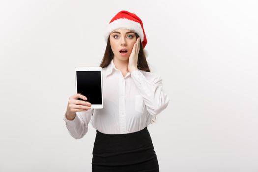 Business Concept - young caucasian business woman in Christmas theme showing digital tablet with surprising facial expression.