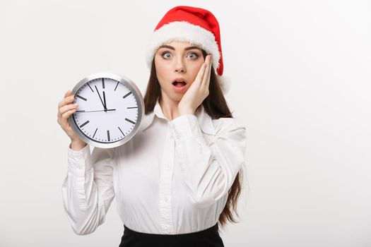 Time management concept - Young business woman with santa hat holding a clock isolated over white background.