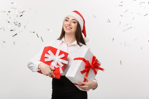Business Concept - Beautiful young caucasian business woman with santa hat holding gift box with confetti celebration background.