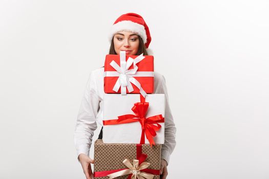 Business Concept - Beautiful young caucasian business woman with santa hat holding a lot of christmas gift boxes with funny face.