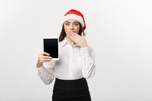 Business Concept - young caucasian business woman in Christmas theme showing digital tablet with surprising facial expression.