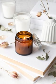 Home decoration and interior. Beautiful burning candles with eucalyptus leaves and dry flowers on pile of white books