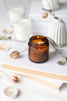 Home decoration and interior. Beautiful burning candles with eucalyptus leaves and dry flowers on pile of white books