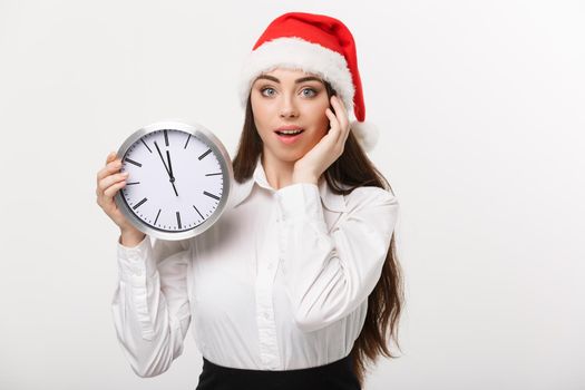 Time management concept - Young business woman with santa hat holding a clock isolated over white background.