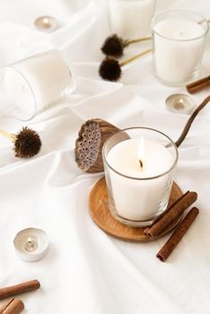 Home decoration and interior. Beautiful burning candles with cinnamon and dry flowers on white fabric background
