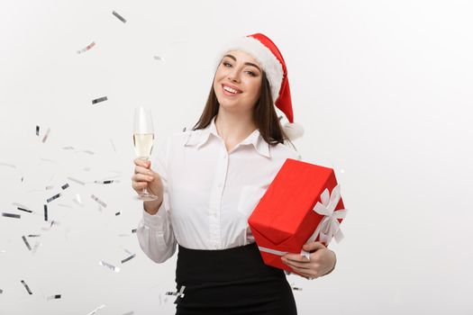 Christmas Concept - young business woman holding champagne and present with confetti background.