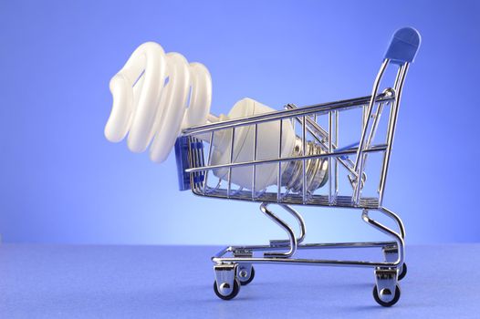 A CFL bulb is inside a miniature shopping cart over a blue background.