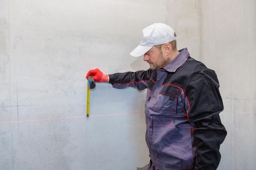 A man, an electrician marks out with a pencil, tape measure and a linear level for drilling holes for sockets