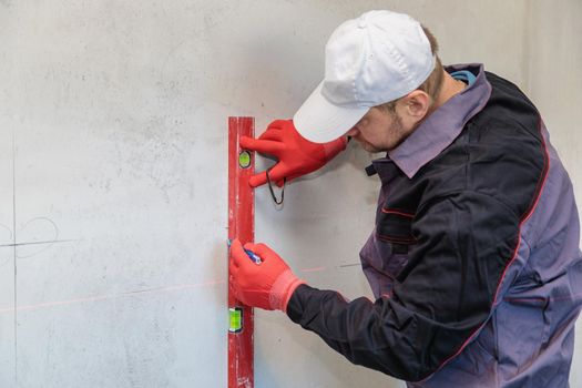 A man, an electrician marks out with a pencil, tape measure and a linear level for drilling holes for sockets