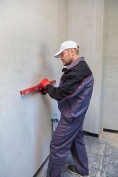 A man, an electrician marks out with a pencil, tape measure and a linear level for drilling holes for sockets