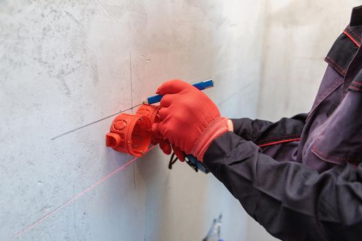 A man, an electrician marks out with a pencil, tape measure and a linear level for drilling holes for sockets