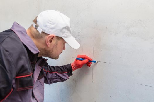 A man, an electrician marks out with a pencil, tape measure and a linear level for drilling holes for sockets