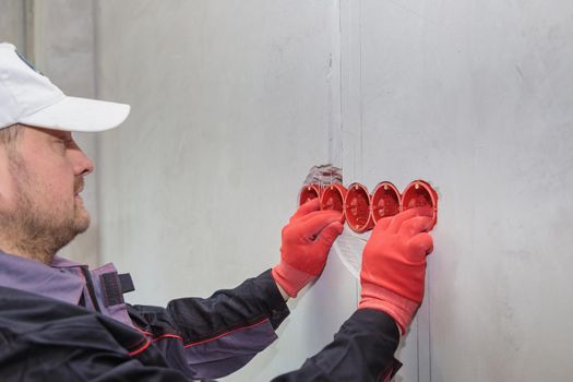 The electrician inserts the plastic box directly into the outlet holes. Close-up