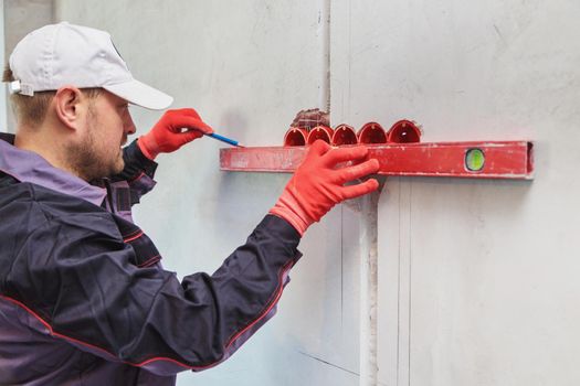 A man, an electrician marks out with a pencil, tape measure and a linear level for drilling holes for sockets