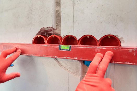 A man, an electrician marks out with a pencil, tape measure and a linear level for drilling holes for sockets