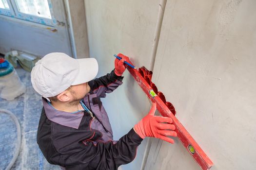 A man, an electrician marks out with a pencil, tape measure and a linear level for drilling holes for sockets