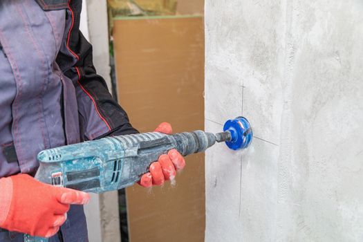 An electrician drills holes for sockets with a diamond core bit. Close-up