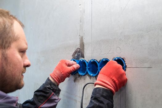 The electrician inserts the plastic box directly into the outlet holes. Close-up