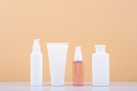 Skin care products in a row on white glossy table against beige background. Beauty and cosmetic concept. Minimalistic still life with beauty products