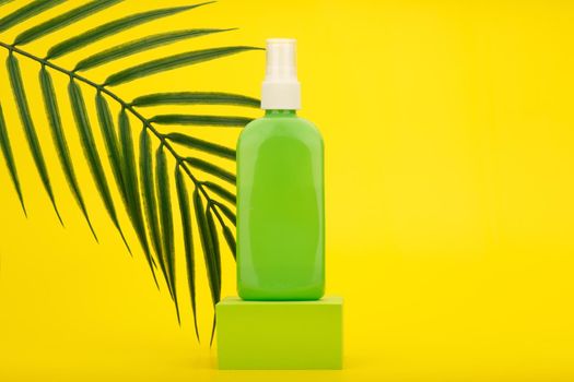 Sunscreen spray with Spf factor in green plastic tube on green square podium against yellow background with palm leaf and copy space. High quality photo