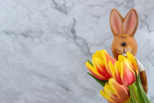 Porcelain easter bunny with yellow red tulip flowers against a grey marbled background