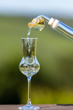 Glass on wooden table with defocused landscape in background get filled with liquor