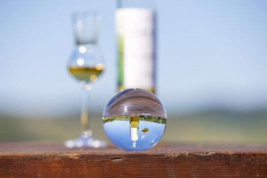 Crystal ball on wooden table with defocused bottle and filled glass in background
