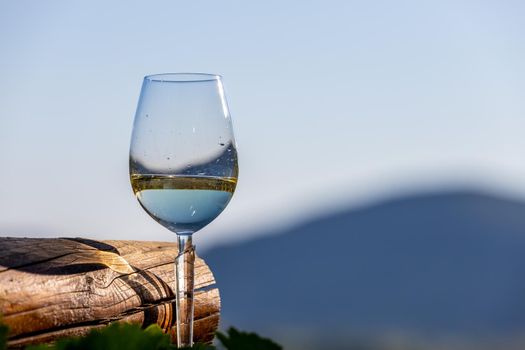 Filled wine glass next to wooden beam and defocused landscape in background