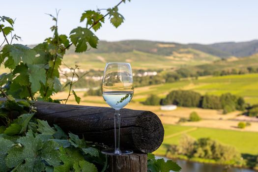 Filled wine glass next to wooden beam and valley of river Moselle in background