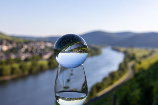 Filled wine glass with crystal ball and valley of river Moselle in background