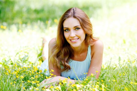 Beautiful young woman in blue dress lying on grass