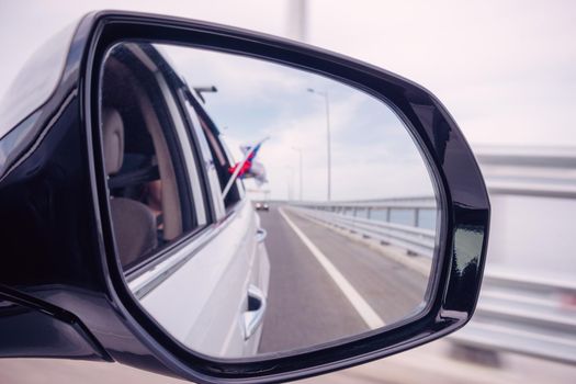 Car mirror with reflection of the road and the Russian flag