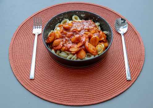 Dischi pasta with sausage, onion and balognese sauce in a black plate on red background. Copy space, No focus, specifically.