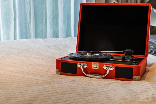 Portable turntable on white bed in bedroom. Selective focus.