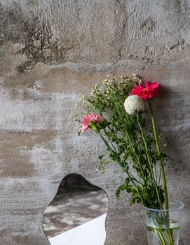 Flowers and mirror on the table with cement wall background with space for your text.
