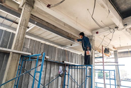 Bangkok, Thailand -  Jan 15, 2015 : Professional painter painting with painting a wall with paint roller and scaffolding with copy space. Selective focus.