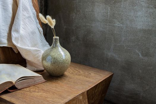 Dried flowers in handmade ceramic vases and book on wooden background. Home decoration, space for text.